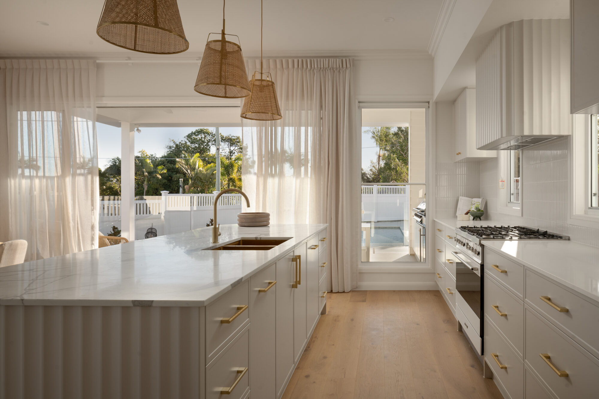 Bright white kitchen with a marble island bench, brass tapware and rattan pendant lights in a Brisbane home