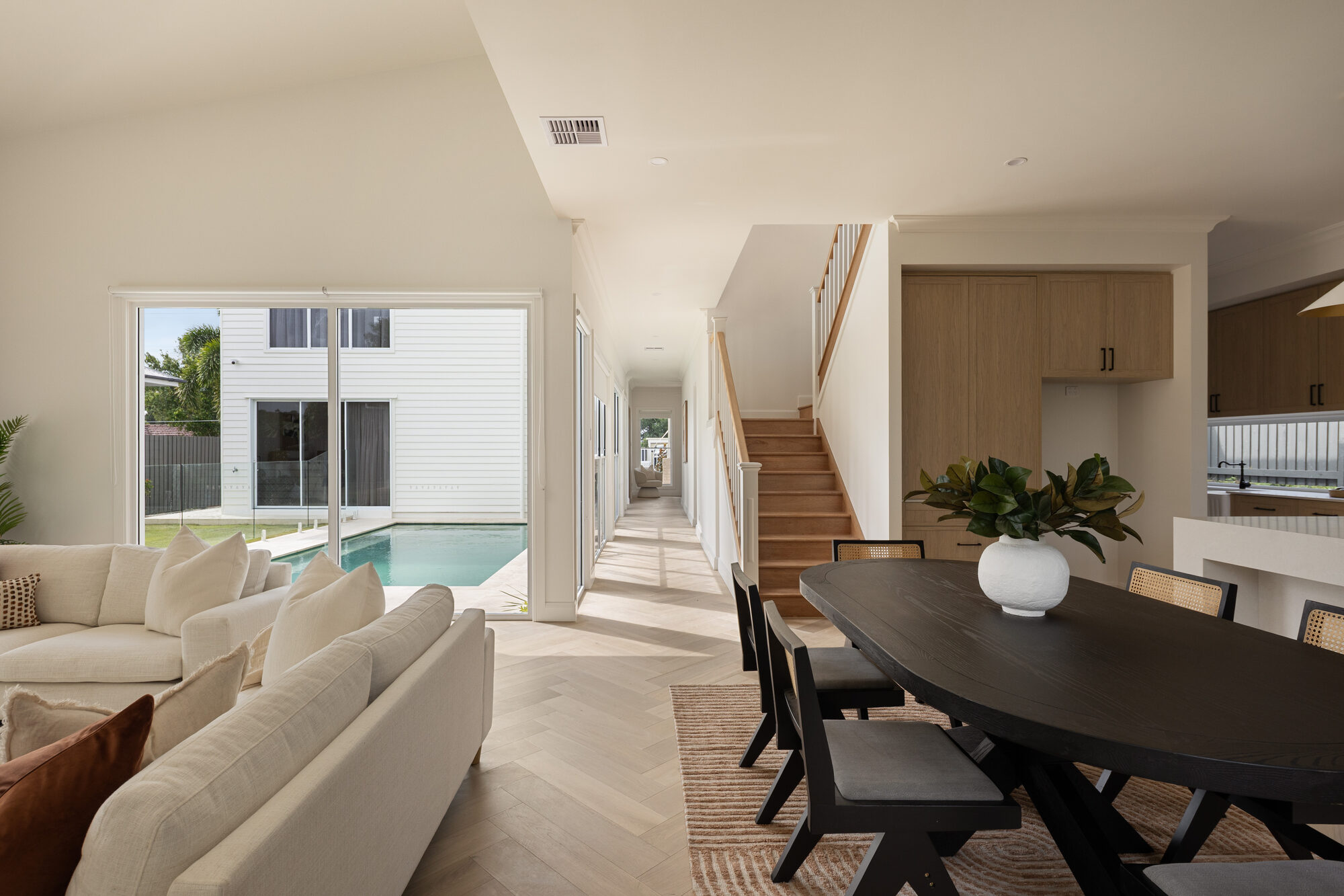 Open-plan living and dining area with herringbone floors looking out to a pool, Brisbane home