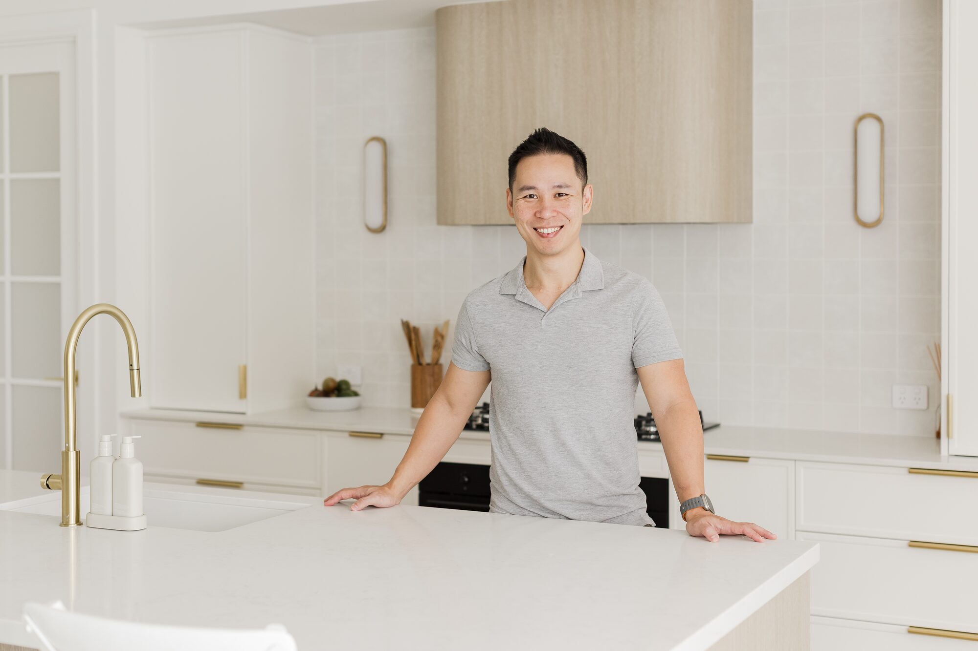 Ian Chan, founder of Imperial Acquisitions Network, standing at a marble island bench in a white kitchen