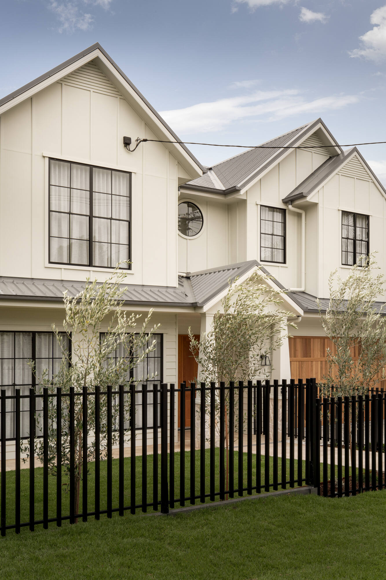 Two-storey cream Hamptons-style home behind a black steel fence, Brisbane