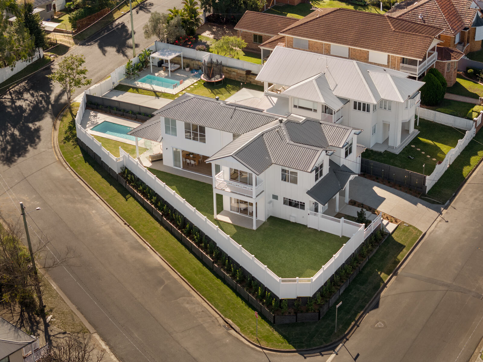 Aerial view of a large white two-storey home with a pool on a Brisbane corner block