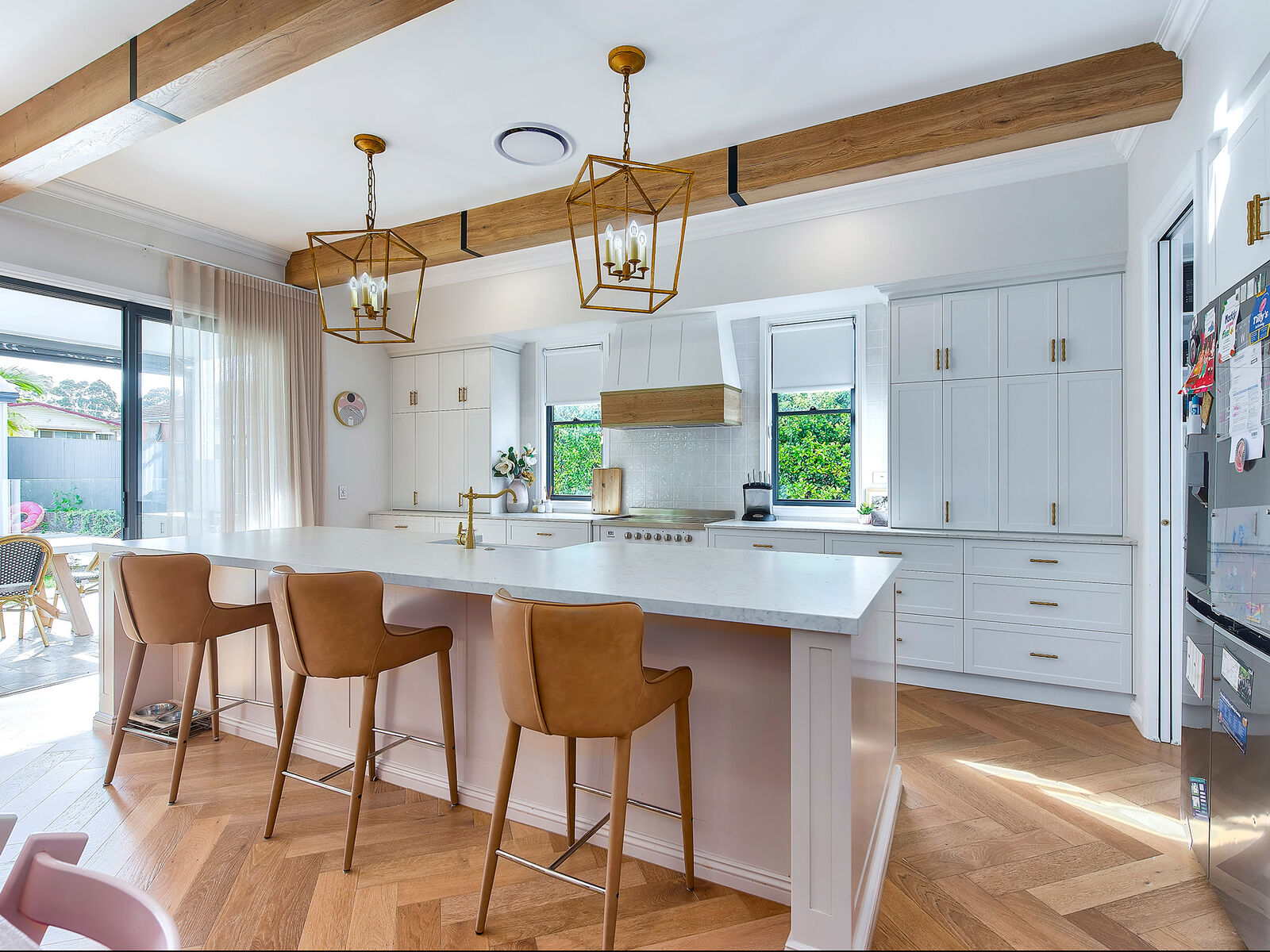 Kitchen with exposed timber beams, brass lantern pendants and a stone island bench with tan leather stools