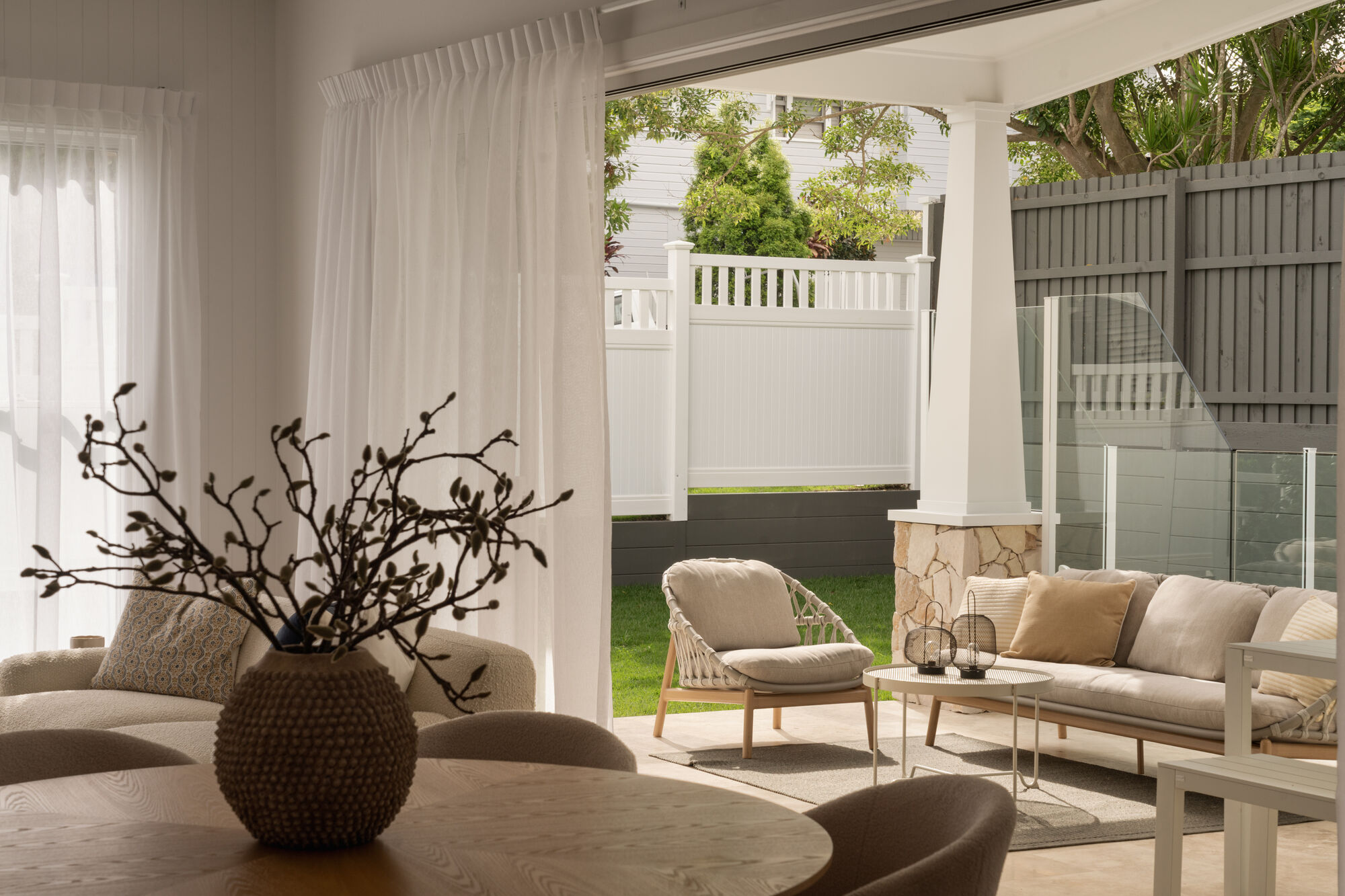 Living area with sheer curtains opening onto a covered patio and landscaped backyard