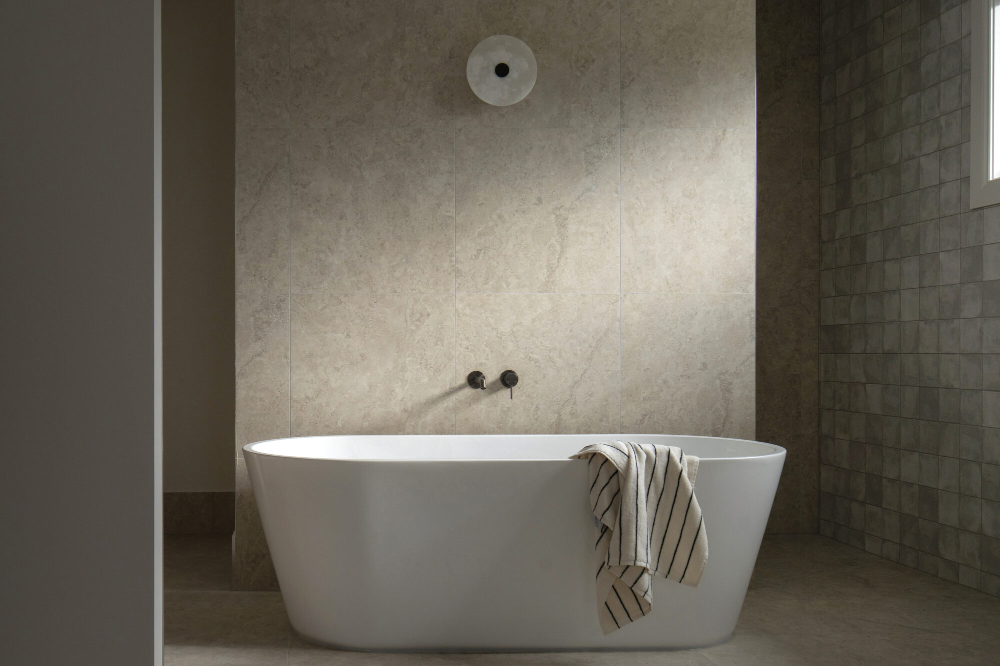 Freestanding white bath against a stone-tiled wall with black wall-mounted tapware