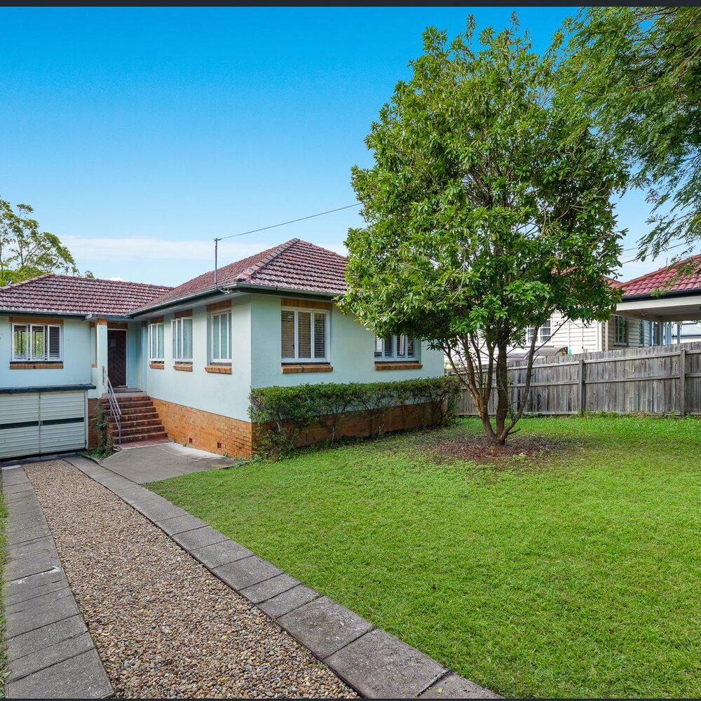 Pale blue post-war home with a tiled roof and a large lawn, Enoggera